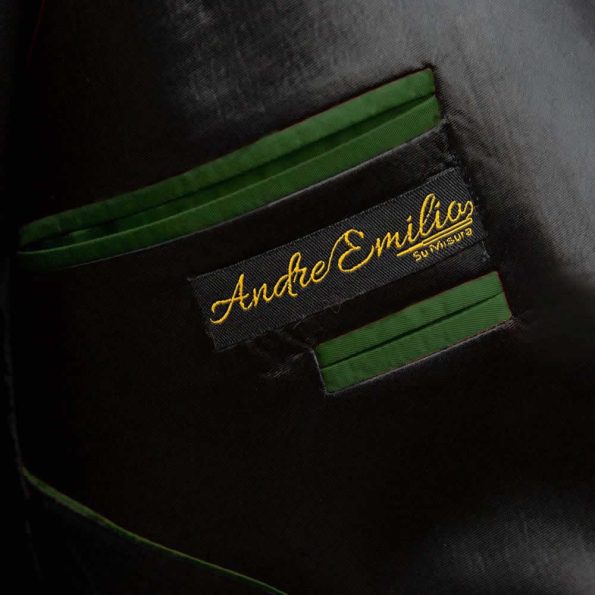 Close-up of the inner side of a black tuxedo jacket with a green lining. The label "Andre Emilio" is stitched in gold on a black tag