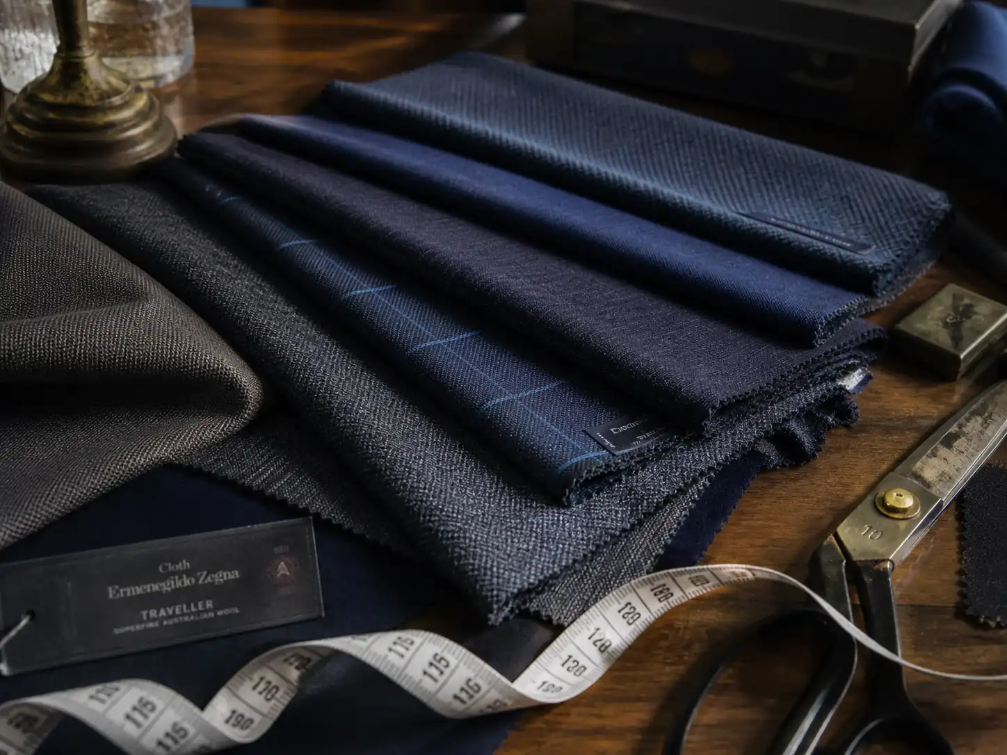 Premium navy and grey custom suit fabric swatches including Guabello cloth with tailor measuring tape on wooden table
