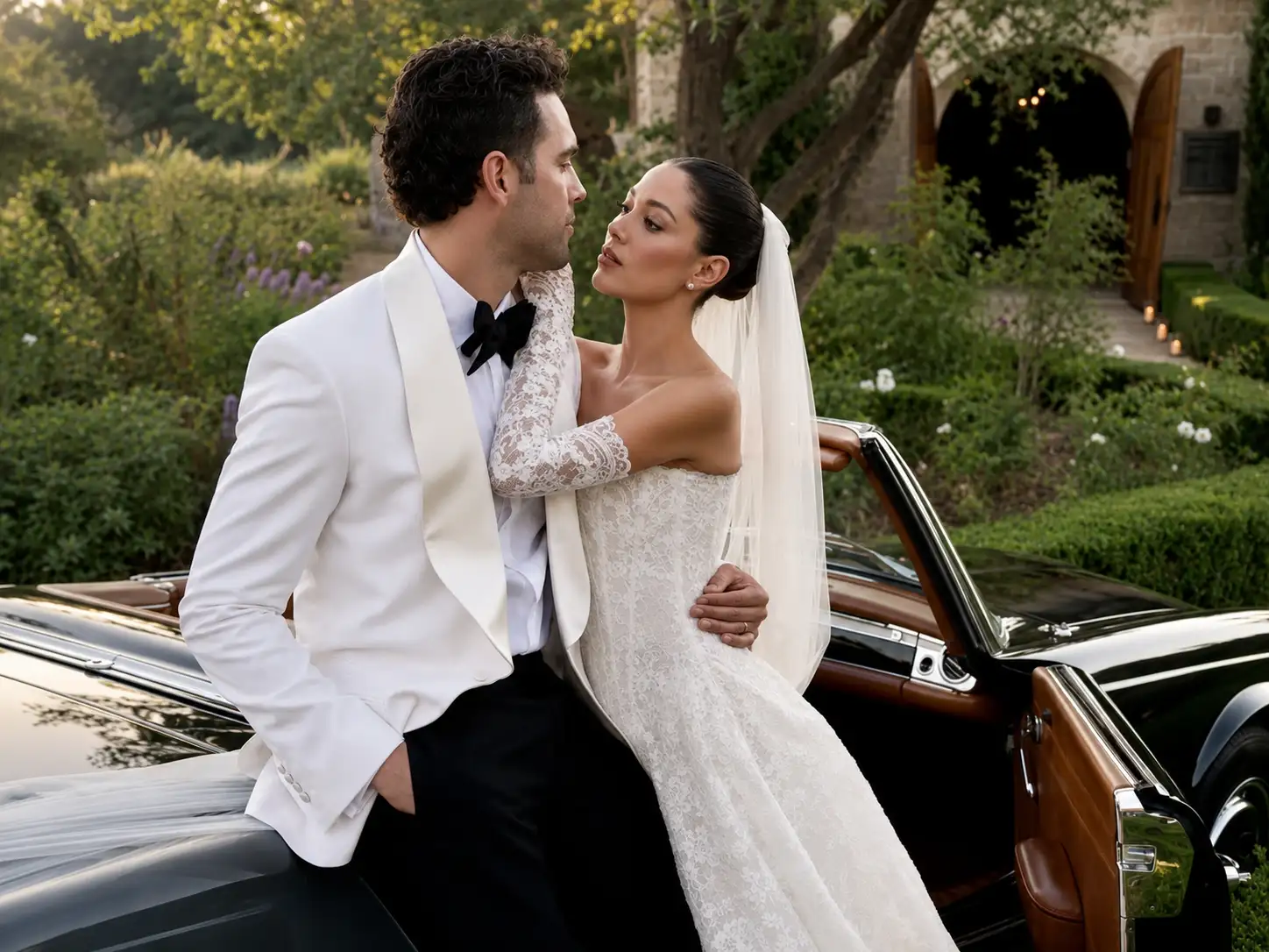 Groom wearing a white dinner jacket with a bride beside a classic convertible wedding car.